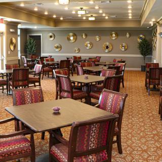 An elegant dining area with neatly arranged tables and chairs, featuring decorative wall art and a carpeted floor.
