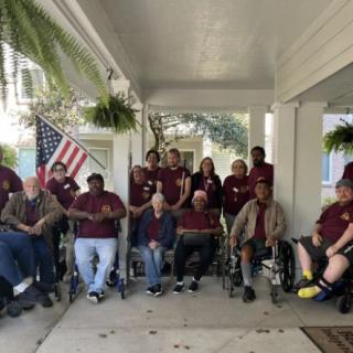 A group of people poses together on a porch with an American flag in the background.