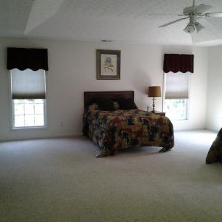 A spacious bedroom with a bed, carpeted floor, and two windows.