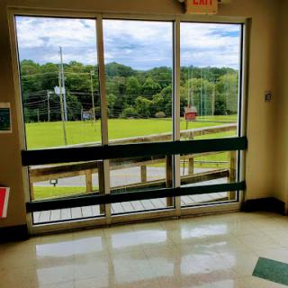 A view through a sliding glass door, showcasing a green landscape under a cloudy sky.