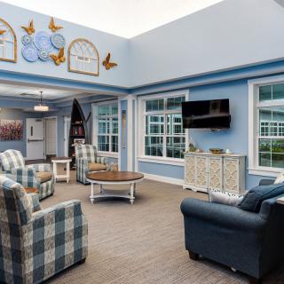 A cozy living room with blue walls, featuring armchairs, a coffee table, and a television.