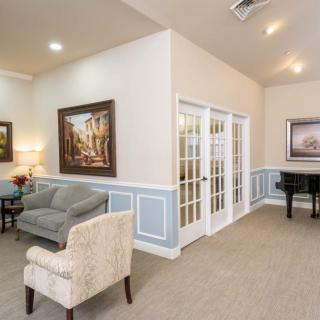 A cozy living room with a sofa, armchair, and piano, featuring artwork and French doors.