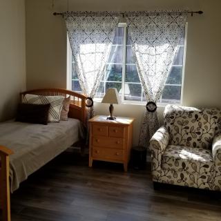 A cozy bedroom with a single bed, armchair, nightstand, and a window adorned with curtains.