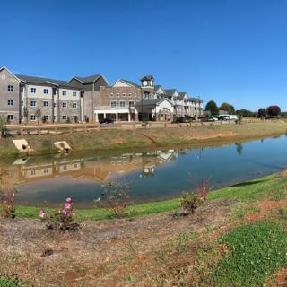A scenic view of buildings reflected in a tranquil lake under a clear blue sky.