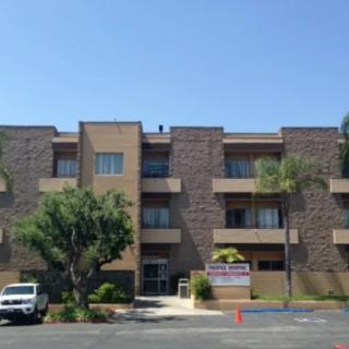 A three-story apartment building with a parking lot and palm trees in front.