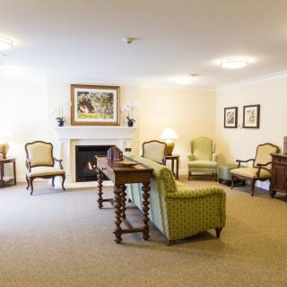A cozy living room featuring a fireplace surrounded by several chairs and a central table, creating an inviting seating area.