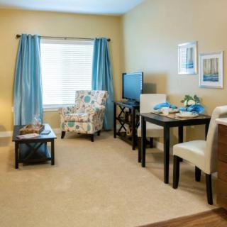 A cozy living room with a dining area, featuring a patterned chair, blue curtains, and a small TV.
