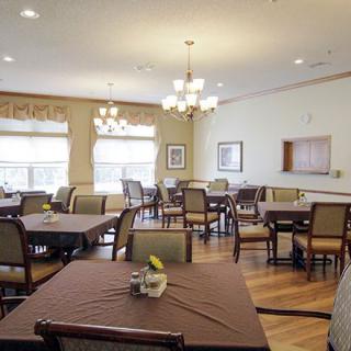 A spacious dining room with neatly arranged tables and chairs, illuminated by chandeliers and natural light from large windows.