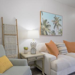 A cozy living room with a white sofa, colorful pillows, and tropical artwork on the wall.