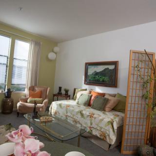 A cozy living room with a sofa, armchairs, and a coffee table, decorated with cushions and a painting on the wall.