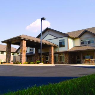 A modern two-story residential building with a covered entrance and surrounding landscape.