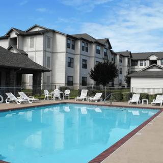 An outdoor swimming pool surrounded by lounge chairs with an apartment building in the background.