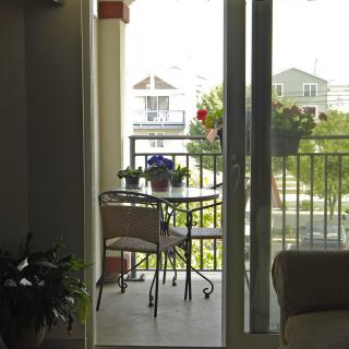 A cozy balcony with a small table and chairs, overlooking a residential neighborhood on a sunny day.