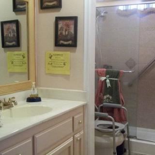 A bathroom featuring a sink with a mirror, a shower equipped with a handrail, and various framed pictures and safety signs on the wall.