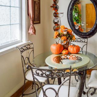 A cozy dining area decorated with autumn-themed items, including pumpkins on a glass table with iron chairs.