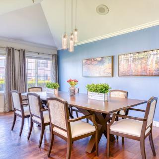A modern dining room with a large wooden table, elegant chairs, and pendant lighting against blue walls.