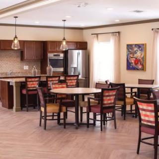 A modern dining area with wooden tables and chairs, adjacent to a kitchen featuring stylish lighting fixtures.