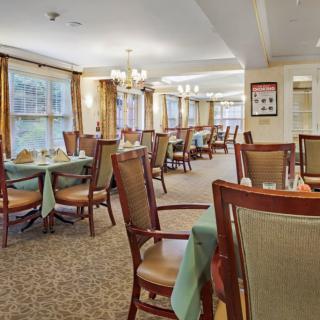 An elegant dining area with neatly arranged tables and chairs, complemented by warm lighting and large windows.