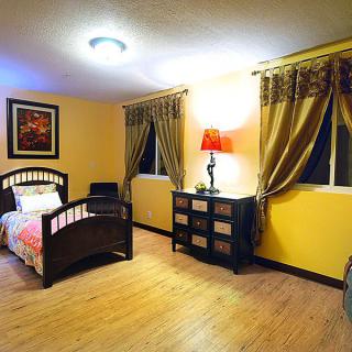 A cozy bedroom with a single bed, dresser, and warm lighting.