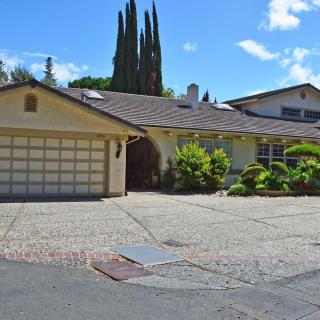 A suburban house with a large driveway and garage, surrounded by greenery under a clear blue sky.