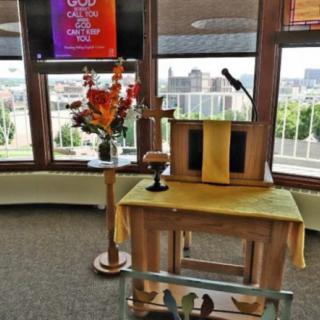 A church podium with a microphone and flower arrangement, set in front of large windows offering a scenic view.