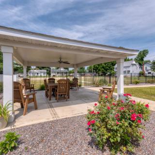 An inviting outdoor gazebo with comfortable seating, surrounded by a landscaped garden and flowers.