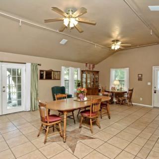 A spacious dining room with wooden furniture and a tiled floor, featuring ceiling fans and large windows.