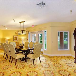 A well-lit dining room with an elegant table and upholstered chairs, featuring stylish lighting fixtures and large windows.
