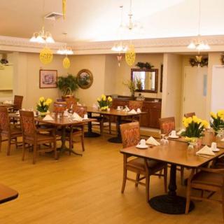 A warmly lit dining area with neatly arranged tables and chairs, featuring elegant decor and floral centerpieces.