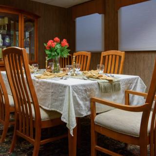 A dining room table set for a meal with wooden chairs and a vase of red roses as the centerpiece.