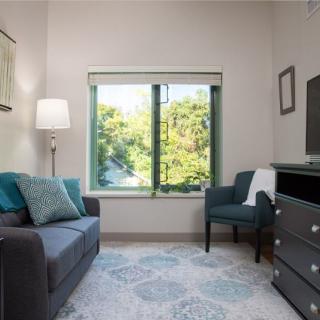 A cozy living room with a grey sofa, an armchair, and a large window offering a view of greenery.