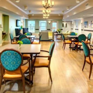 A brightly lit dining area with elegant chairs and tables, featuring a wooden floor and decorative lighting.