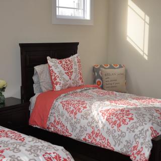 A cozy bedroom with twin beds, featuring floral-patterned bedding and sunlight streaming through the window.