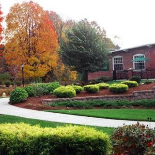 A scenic view of a landscaped garden with vibrant autumn foliage and a pathway leading to a brick building.