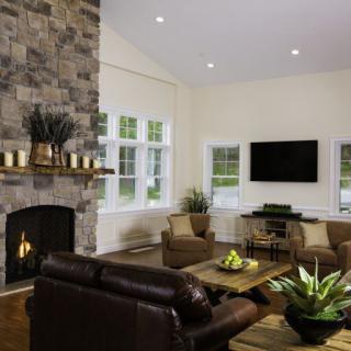A cozy living room featuring a stone fireplace and leather seating, with a television mounted on the wall.