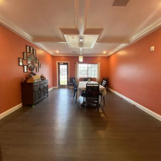 A spacious dining room with vibrant orange walls, featuring a central table and chairs, wood flooring, and decorative items on a sideboard.
