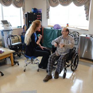 A healthcare worker engages with an elderly person in a wheelchair, promoting interaction and support in a rehabilitation setting.