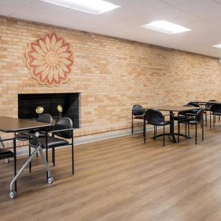 A modern dining area with tables, chairs, and a fireplace against a brick wall.