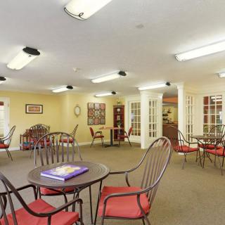 A well-lit indoor seating area with several round tables and red cushioned chairs on a carpeted floor.