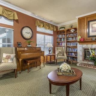 A cozy living room with traditional decor featuring a piano, bookshelves, and a fireplace.