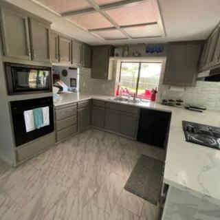 A modern kitchen with gray cabinets, featuring an oven, stove, and sink by the window.