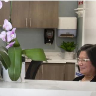 A woman sitting behind a reception desk with orchids in the foreground.