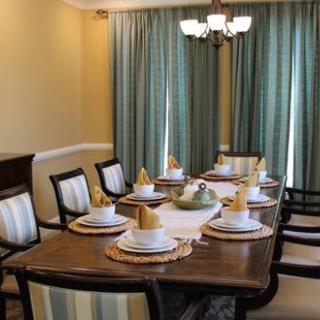 A well-set dining table with elegant place settings and chairs, complemented by teal curtains and a classic chandelier.