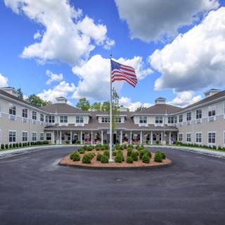 A large building with a circular driveway and an American flag in the center, set against a backdrop of a cloudy sky.