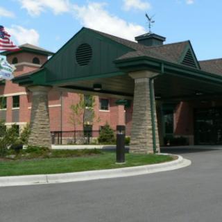 A brick building with a green-roofed entrance and driveway, featuring an American flag in the background.