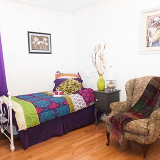 A cozy bedroom with colorful bedding, an armchair draped with a blanket, and decorative wall art.
