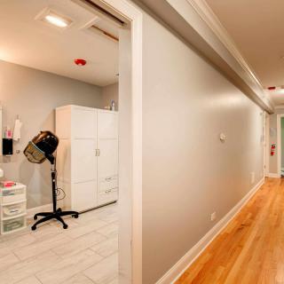 A hallway leading to a hair salon room with a dryer chair and cabinets.