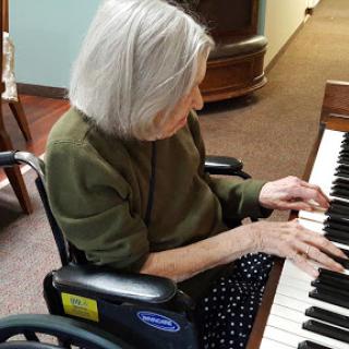 An elderly woman in a wheelchair enjoying playing the piano.
