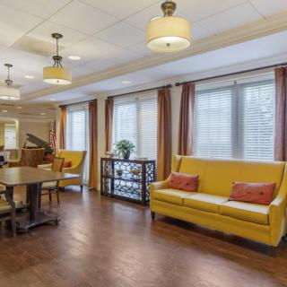 A cozy living room with bright yellow sofas, a piano, and large windows adorned with curtains.