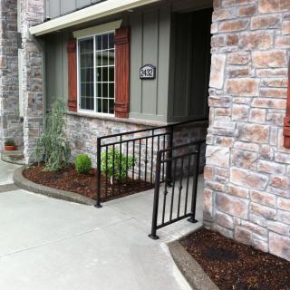 A house entrance with a ramp and railing, featuring a stone facade and landscaped garden.